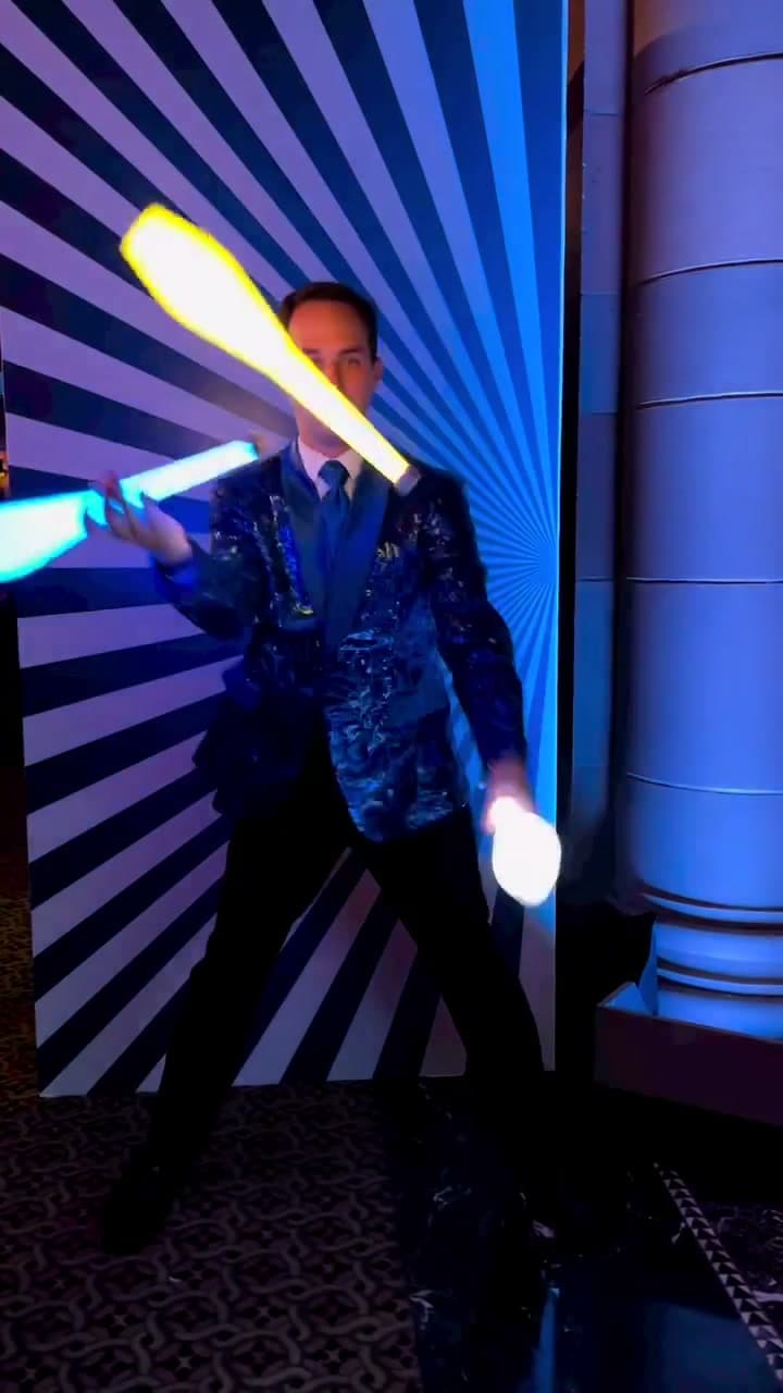 LED juggler in sequined jacket spinning illuminated pins on a stage at a private event