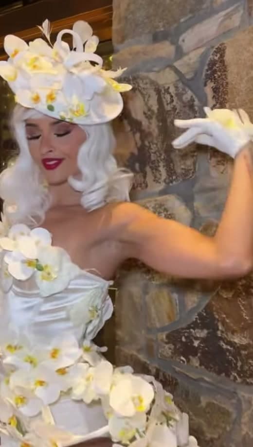 Orchid clad showgirl performer in white floral costume against a stone wall at a luxury New York event