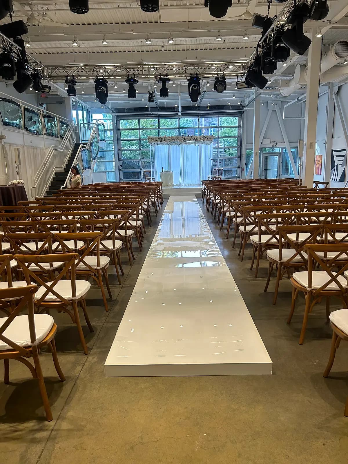 Custom white ceremony runway and stage build under a production lighting truss at an industrial loft wedding venue