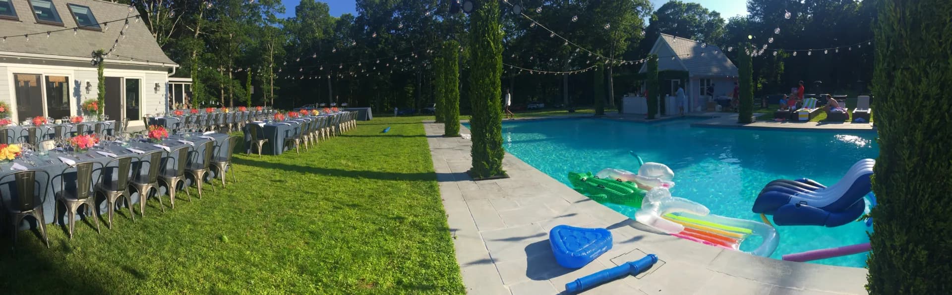 Daytime Hamptons estate pool party with long dining tables on the lawn and a pool, planned by Nicholson Events