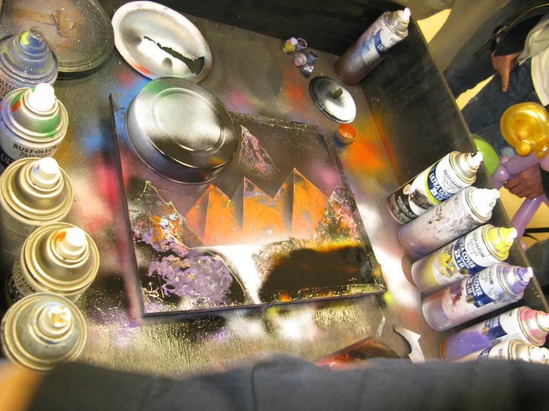Spray paint artist work station with paint cans and a cosmic mountain design taking shape at a live spray art station