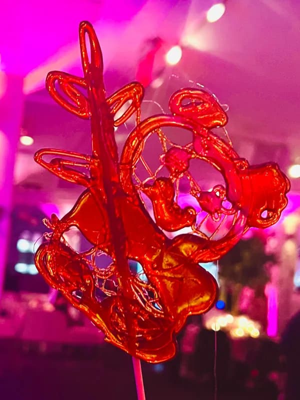 Hand-pulled sugar candy sculpture in red and gold on a stick under colorful event lighting