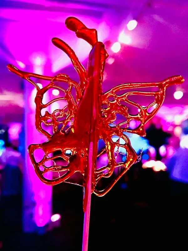 Hand-pulled candy sculpture shaped like a butterfly, glossy amber sugar art on a stick