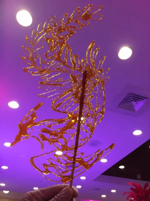 Live candy sculpture artist holding a finished golden sugar art piece at an event