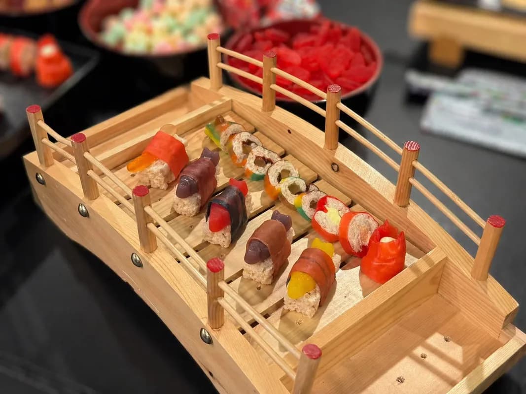Candy sushi rolls arranged on a wooden bridge display tray at an event dessert table