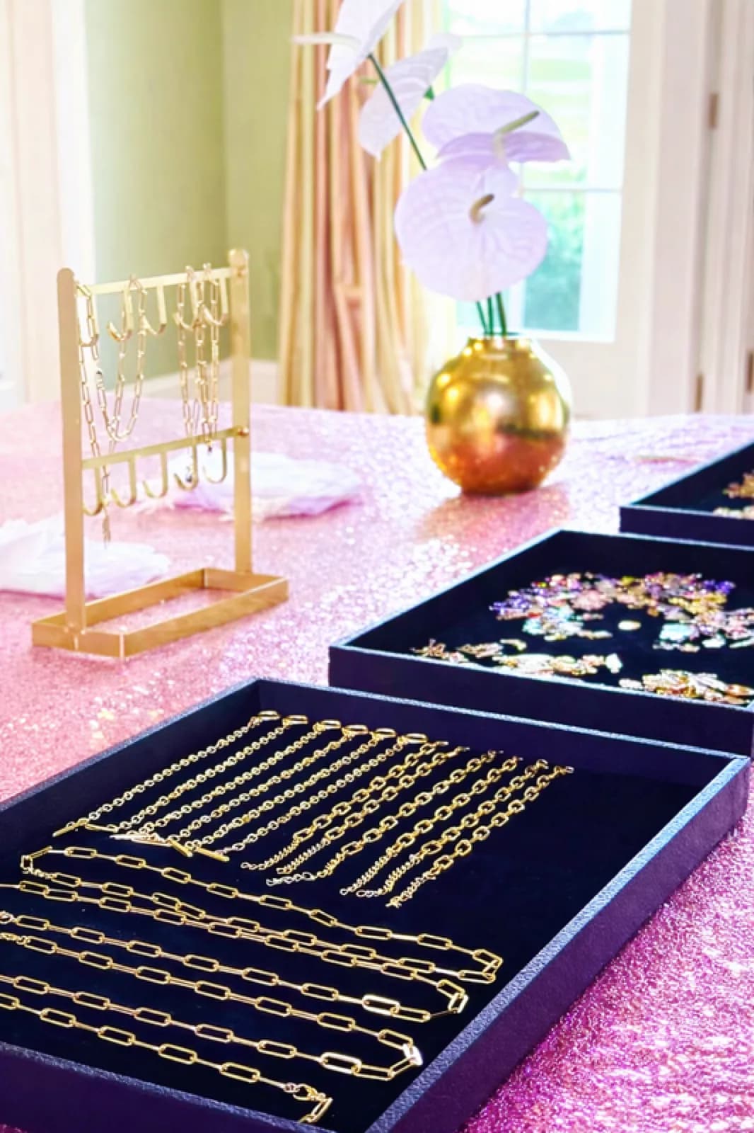 Gold chain necklaces and bracelets displayed in velvet trays on a styled charm bar table