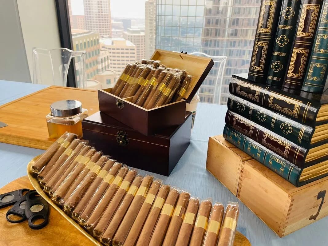 Rows of hand-rolled cigars on a tray beside leather cigar boxes with a city skyline view in the background