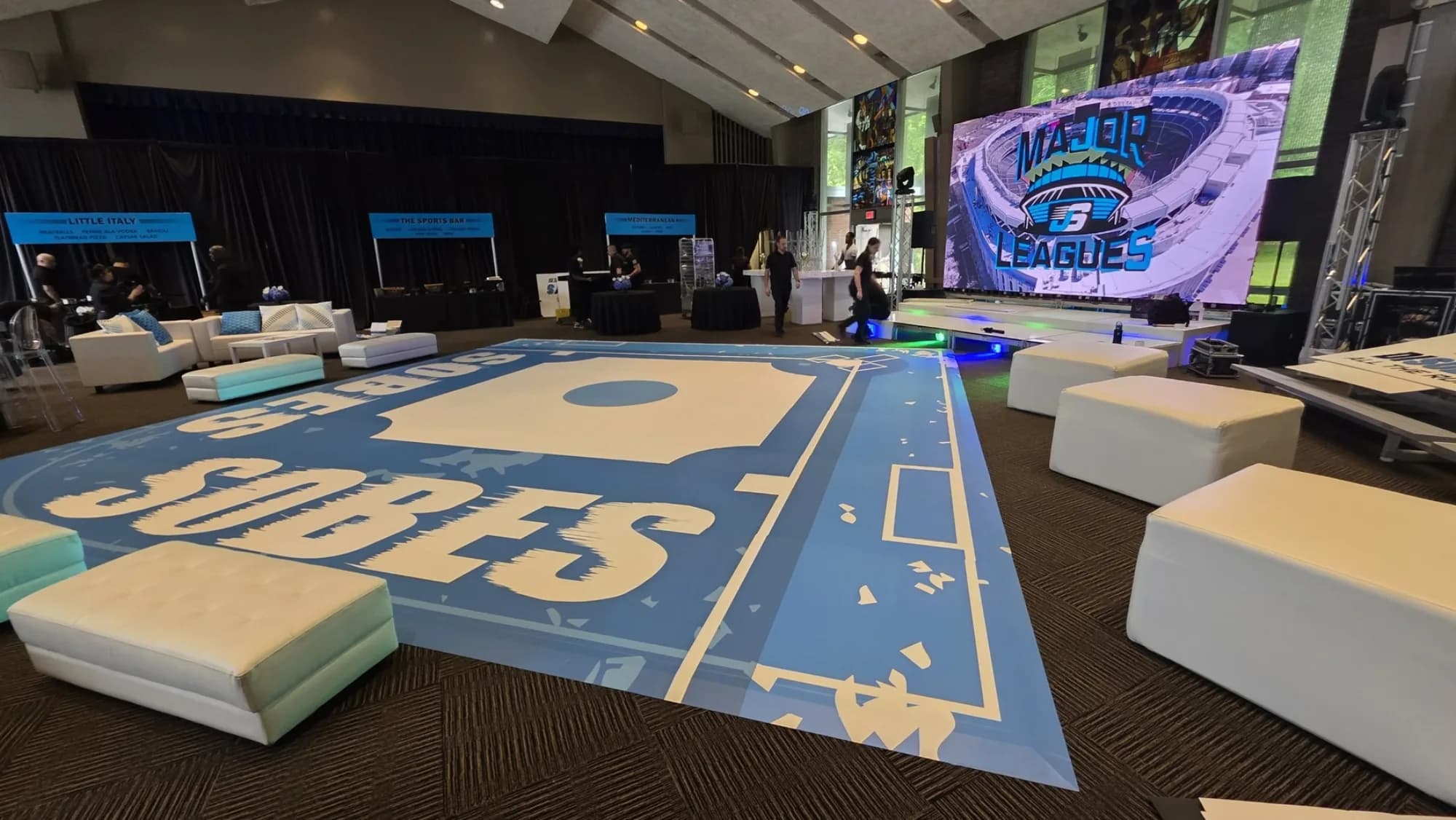 Custom vinyl dance floor wrap displaying a personalized event name in large white letters on a light blue surface inside a tented venue