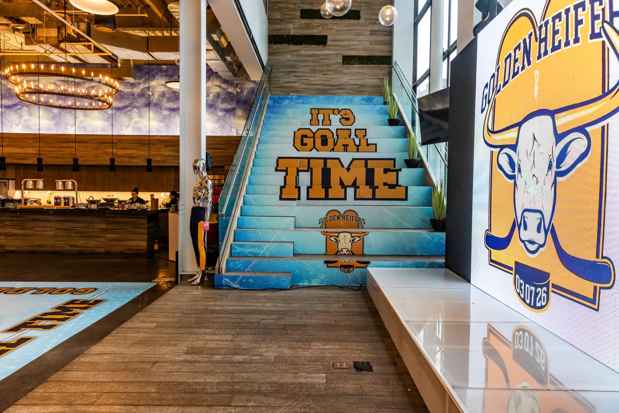 Custom vinyl stair and floor wrap installation at a modern venue showing a bold event theme in blue and gold with a custom mascot design