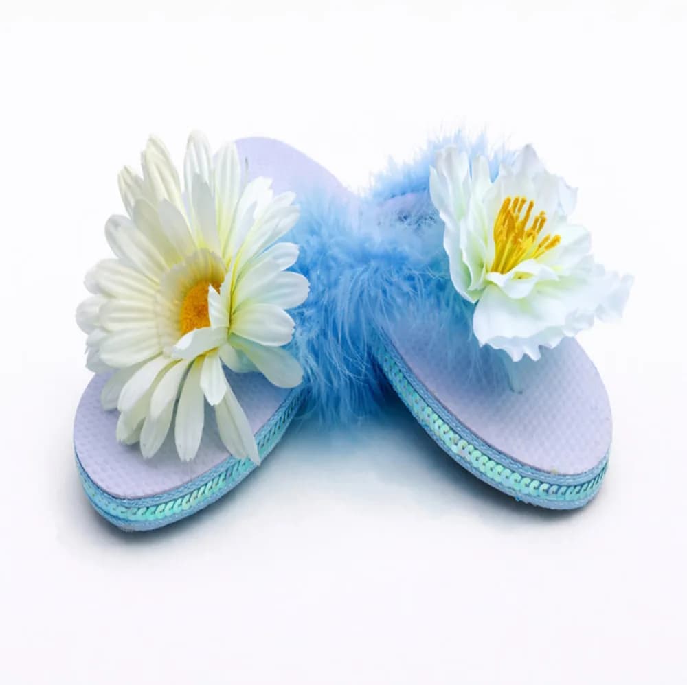 Finished white flip flops decorated with pale blue feathers and daisy flowers, a wearable keepsake from the decorate flip flops station
