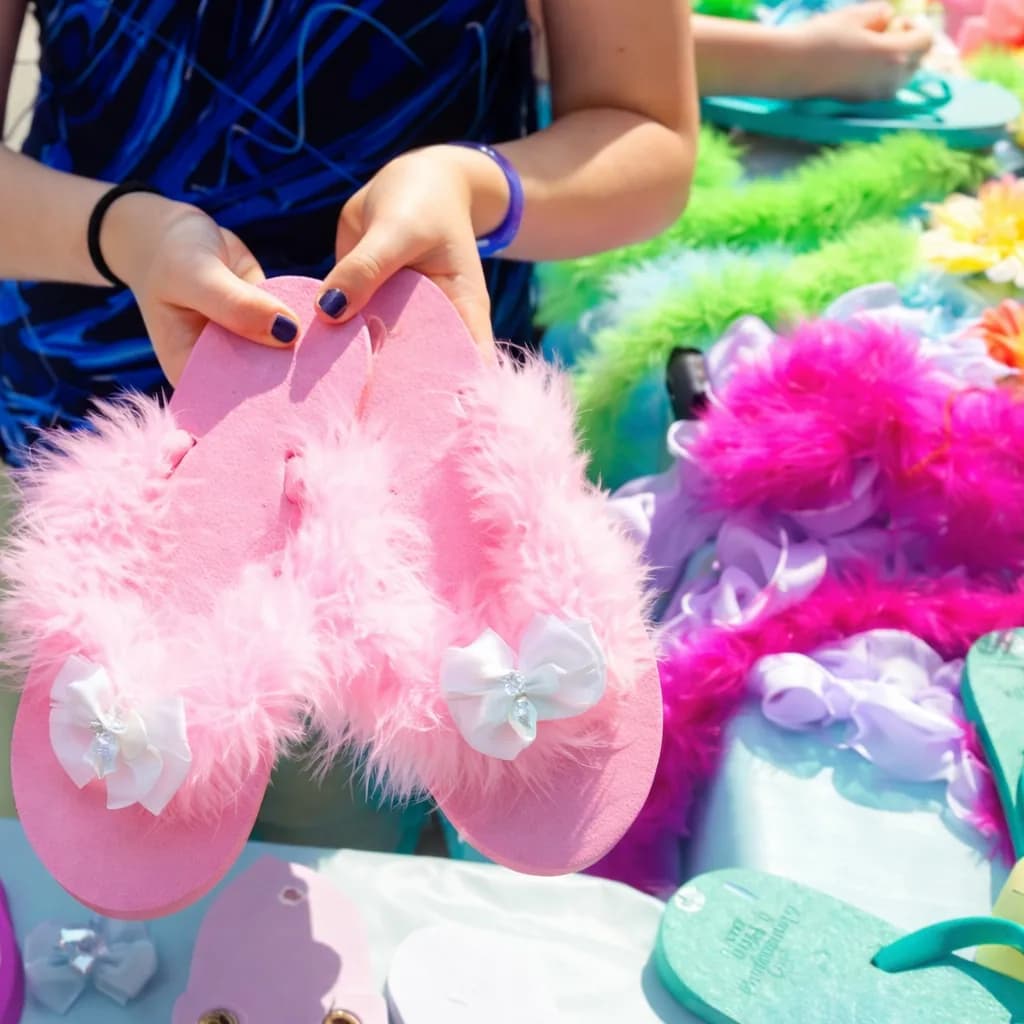 Guest holding a pair of pink feathered flip flops with white bow accents at a decorate flip flops station