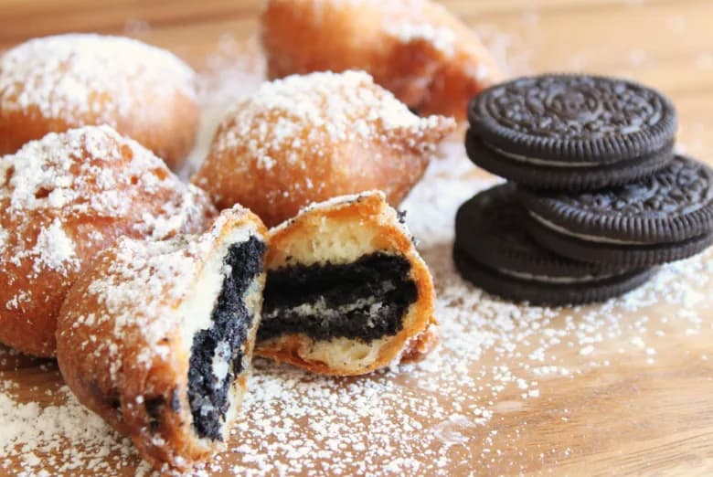 Deep fried Oreos on a wood board next to classic Oreo cookies, split open to show the fried batter and cream filling