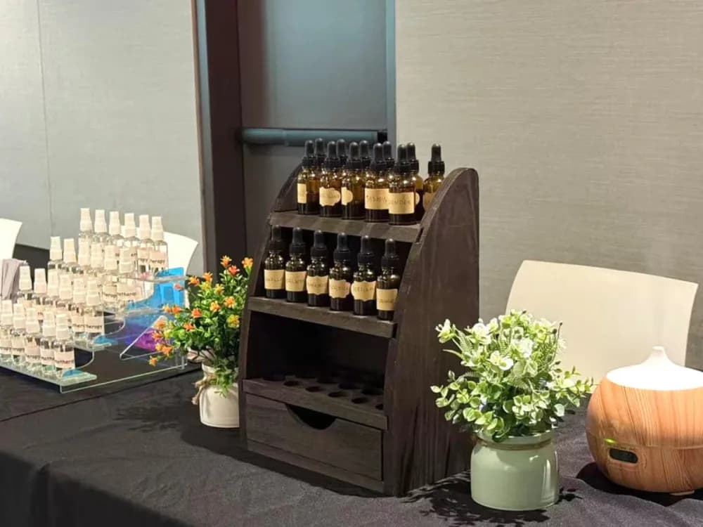 Wooden display rack of amber essential oil dropper bottles alongside spritzer bottles and a diffuser at an event wellness station