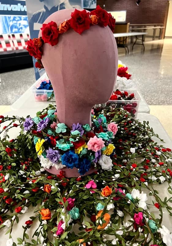 Mannequin bust wearing a red rose flower crown displayed beside bins of loose silk blooms at a flower crown station
