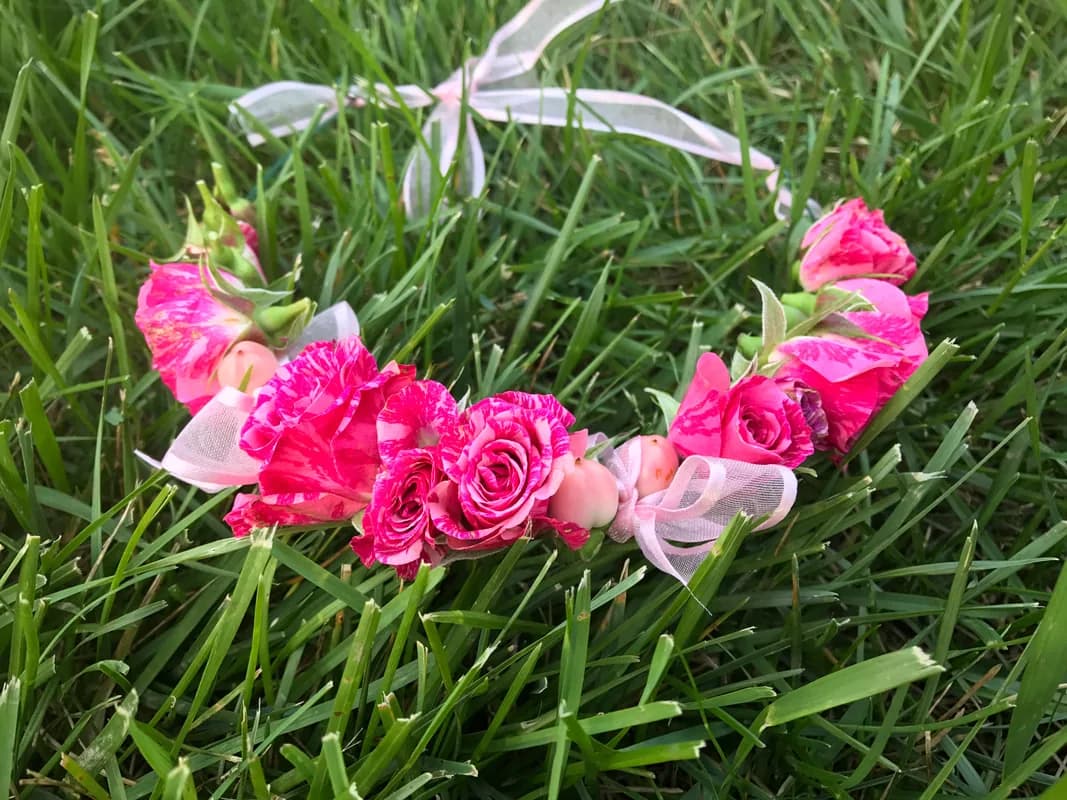 Finished silk flower crown in hot pink tones with sheer ribbon ties resting in the grass