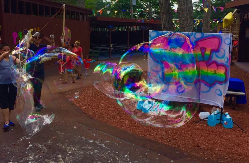 Giant bubble artist and children creating an enormous rainbow-toned bubble tunnel at an outdoor party