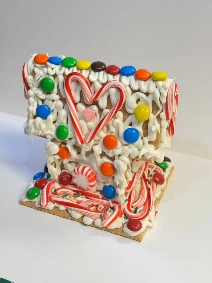 Decorated gingerbread house wedge topped with colorful candy and a candy cane heart, a keepsake from the gingerbread house station