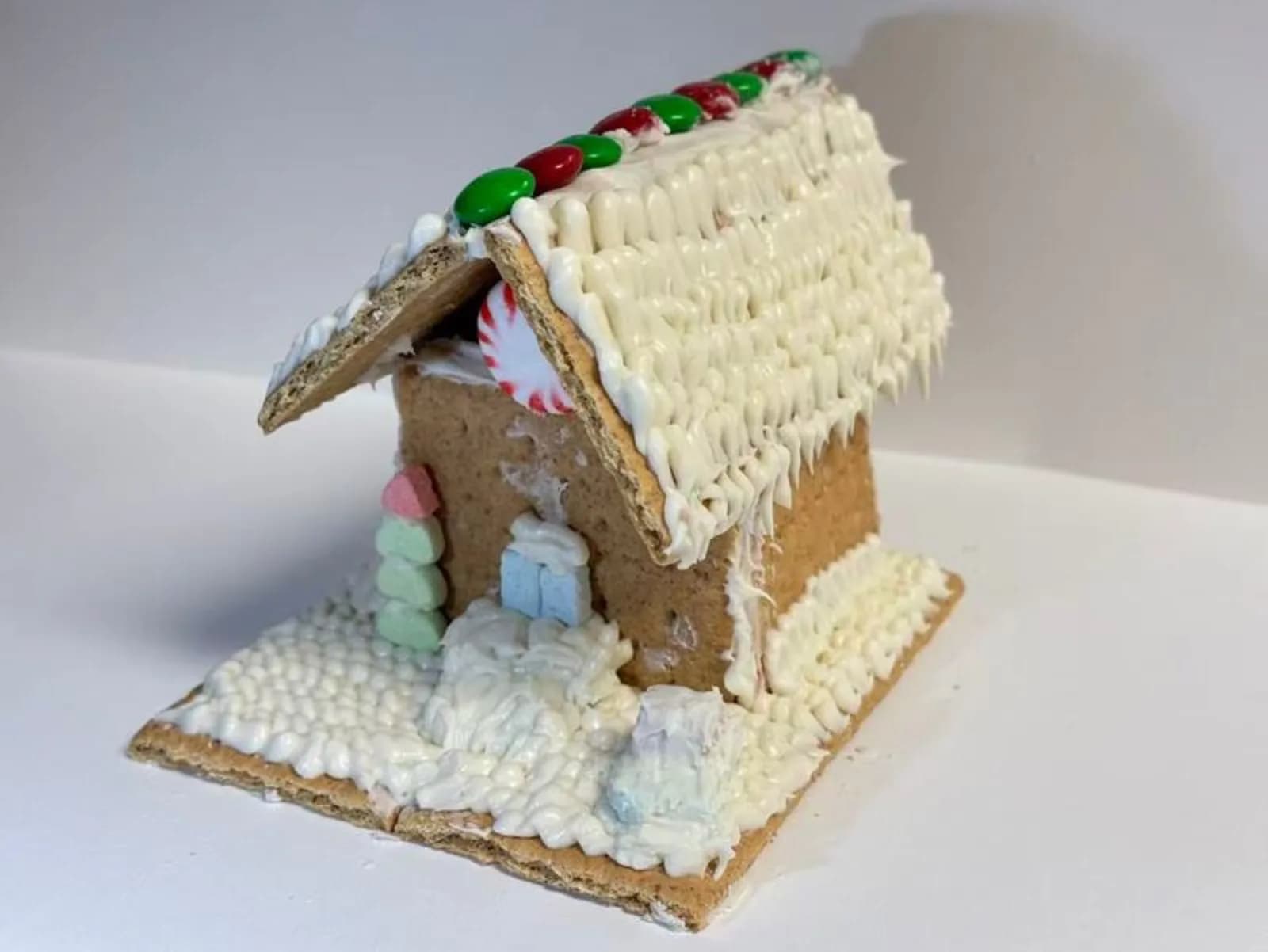 Close-up of a decorated gingerbread house roofline lined with red and green candy and dripping white icing