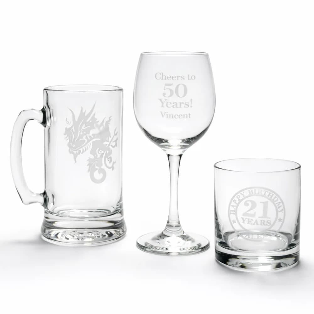 Etched dragon mug, wine glass reading Cheers to 50 Years, and personalized rocks glass, examples of custom engraving from the glass etching station