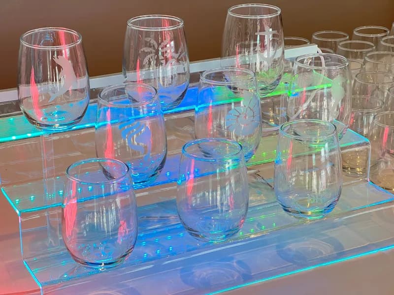 Close-up of etched stemless wine glasses with nautical designs illuminated by colorful lighting at a glass etching station