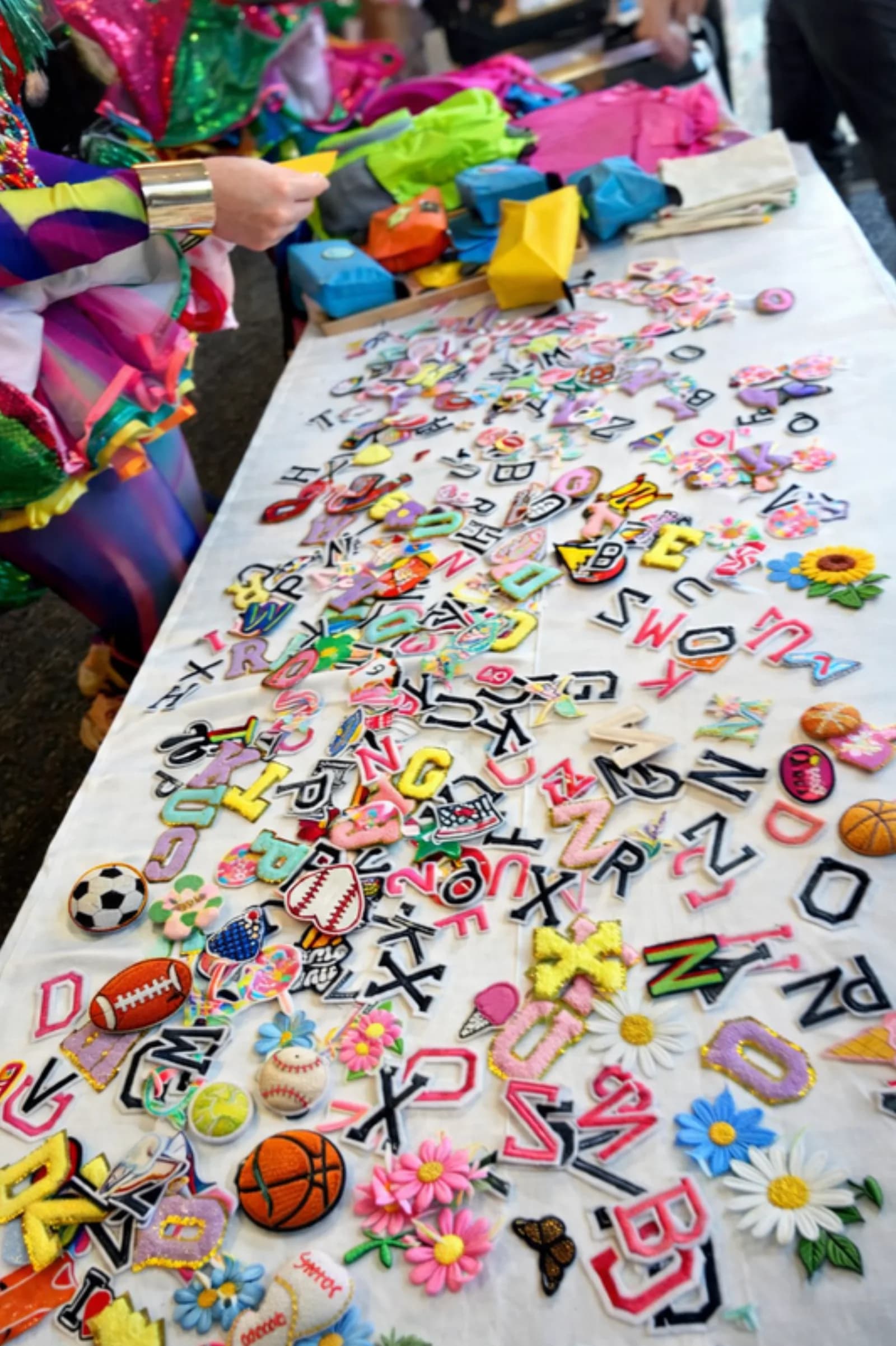 Hundreds of iron-on patch designs, including letters, sports icons, and florals, spread across a table for guests to choose from at the iron patch station