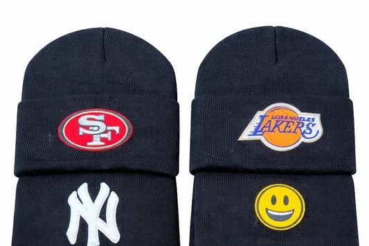 Two knit beanies customized with iron-on sports team logo patches and a smiley face, showing the design variety available at the iron patch station