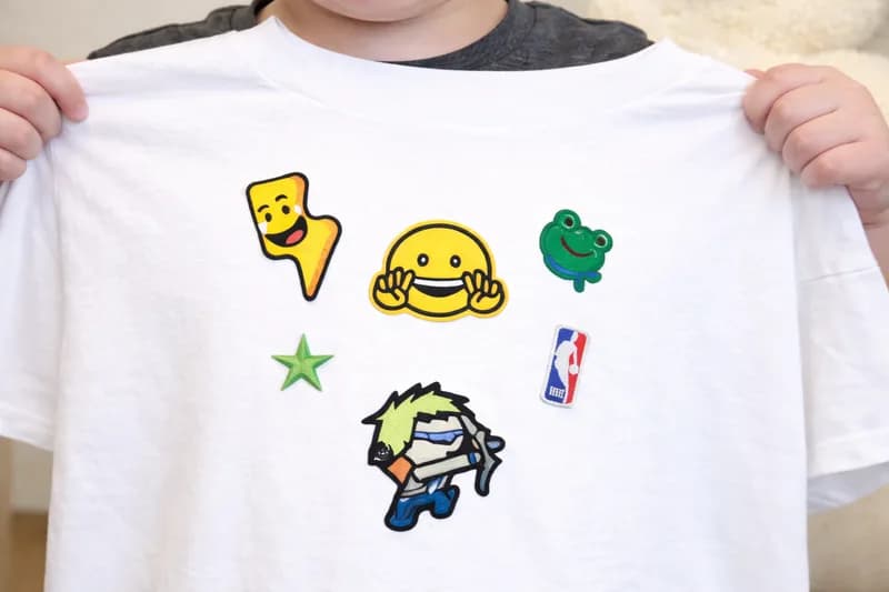 Guest holding open a white t-shirt customized with iron-on character, star, and smiley patches from the iron patch station