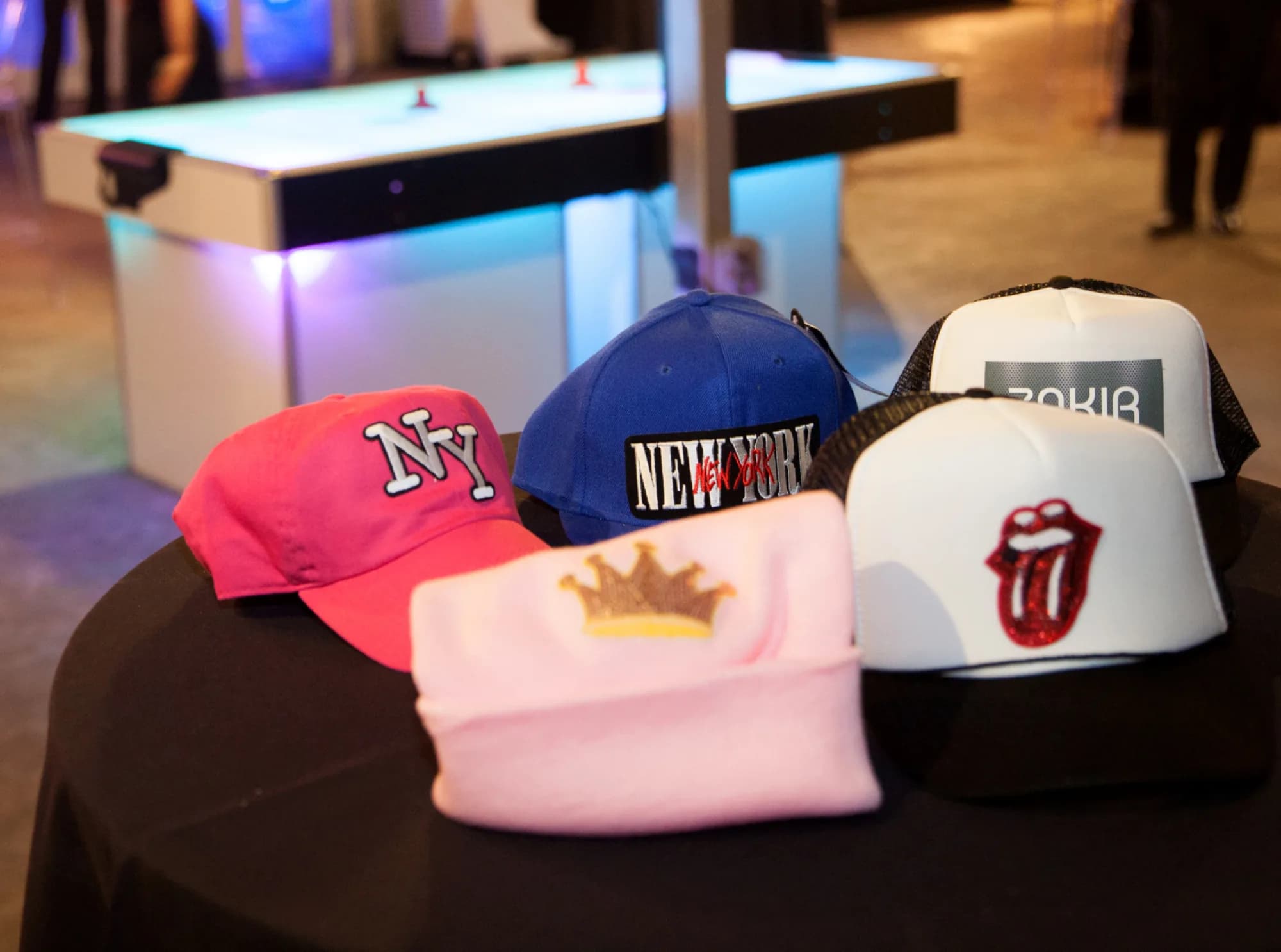 Finished custom hats on a table at a live event, featuring personalized patches and embroidery in red, blue, and pink