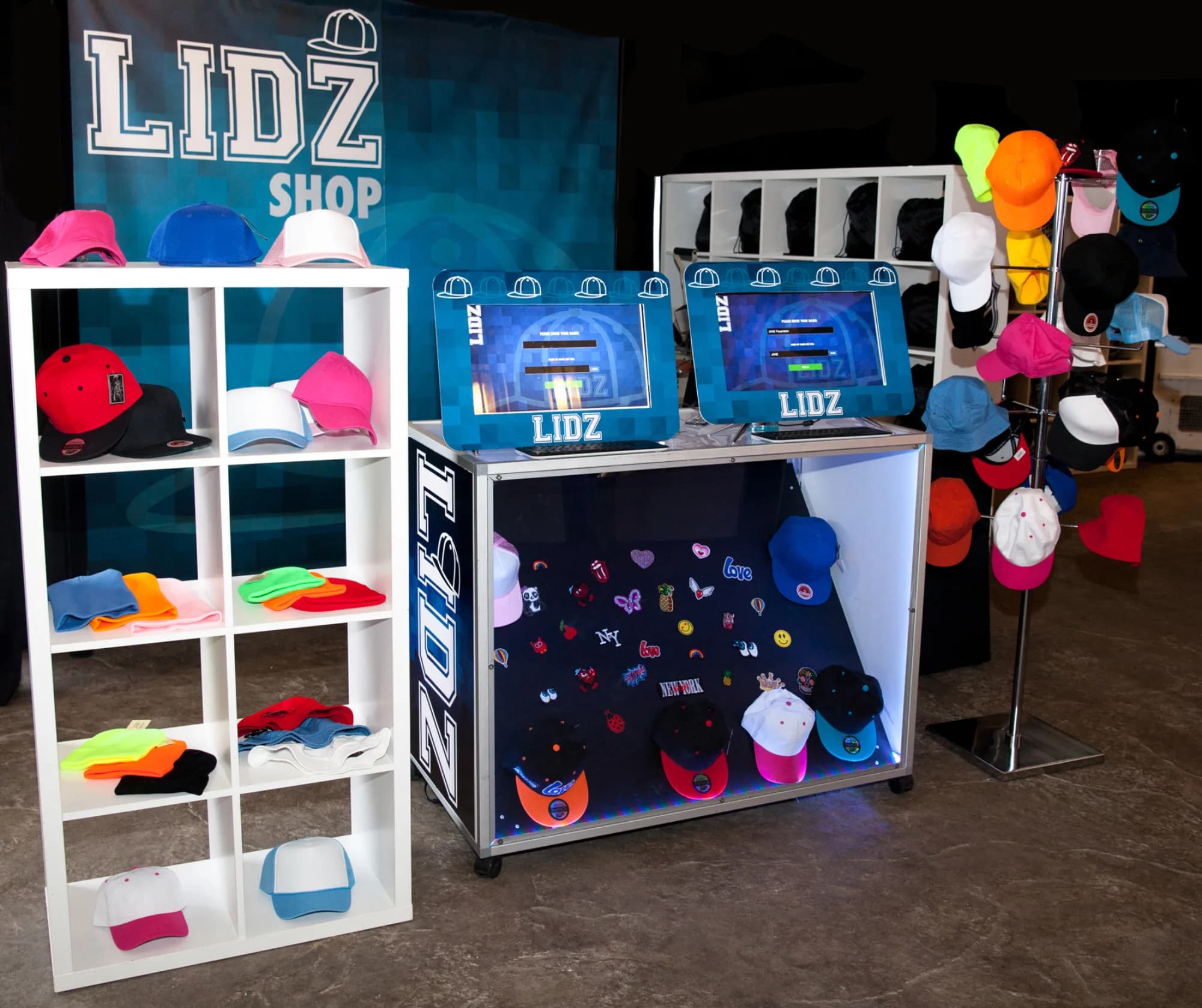 Custom hat personalization station with a wall of colorful baseball caps and beanies alongside a dual-screen kiosk at a New York party