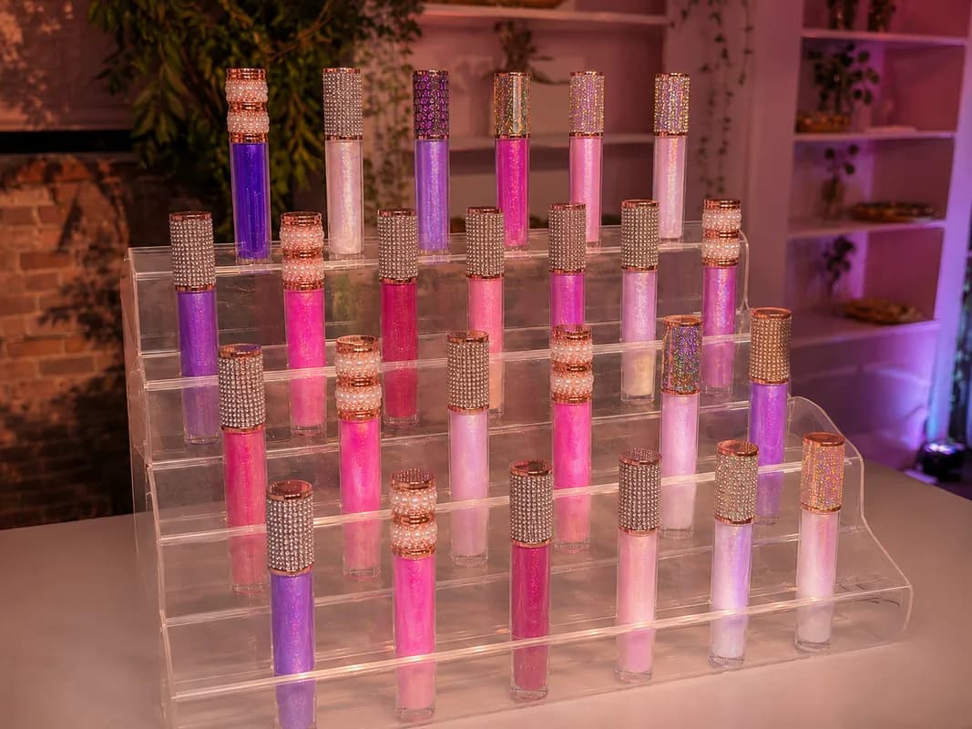 Tiered display of glam lip gloss tubes with rhinestone and pearl caps at an evening lip gloss bar station