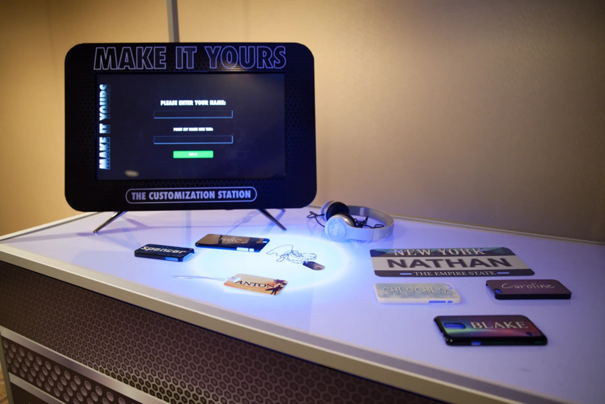 Make It Yours customization kiosk with illuminated table displaying personalized phone cases and license plates at a New York event