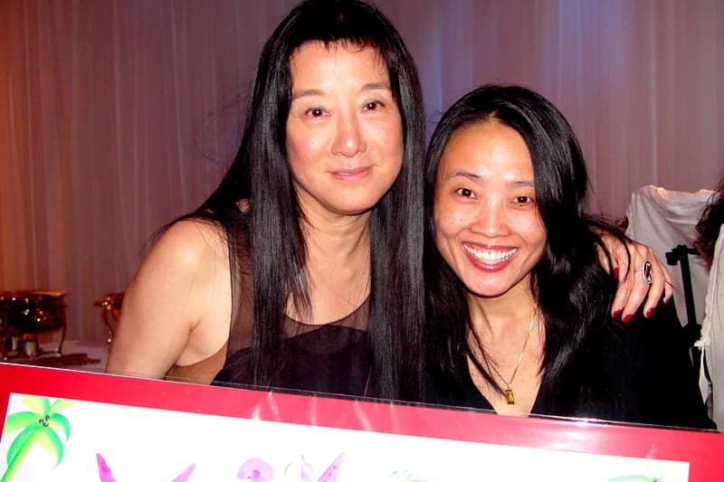 Two guests smiling together while holding up a finished name painting in a red frame, decorated with butterflies and palm tree imagery, from the name painting station
