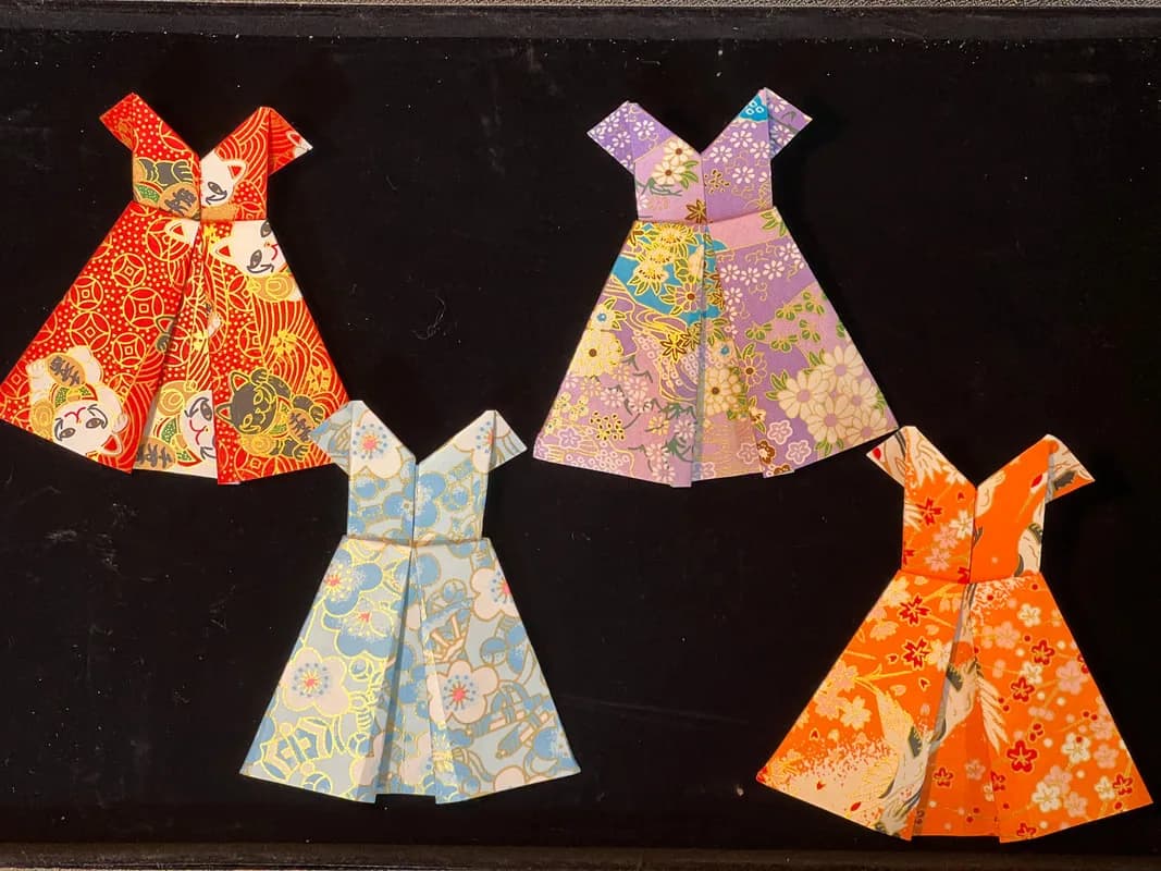 Four Japanese-paper origami dresses in red, purple, blue, and orange floral patterns, folded keepsakes from the origami station