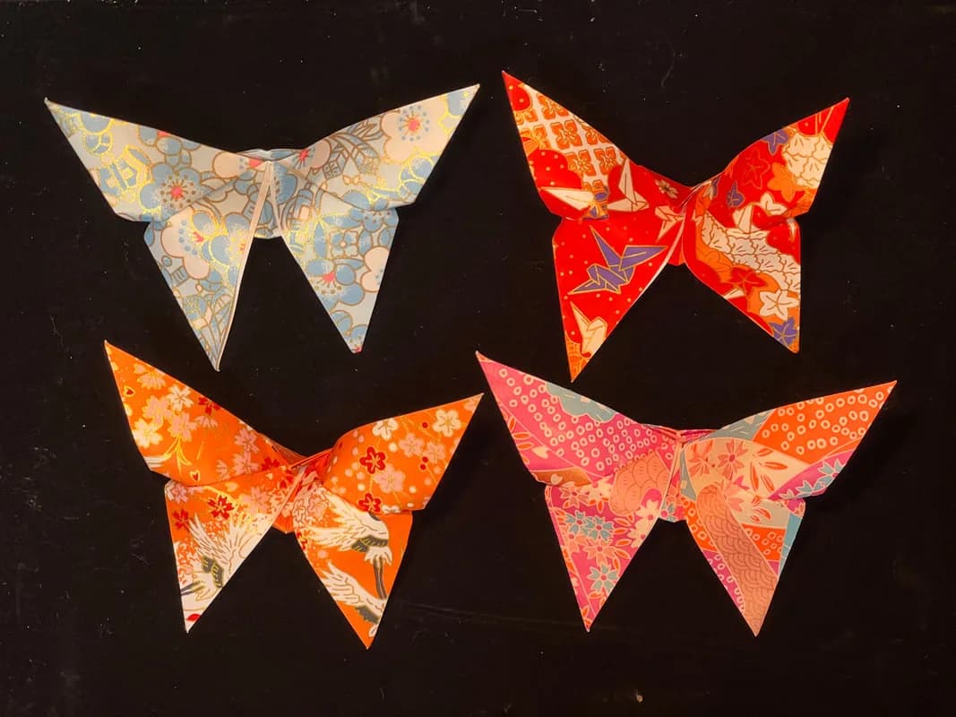 Four Japanese-paper origami butterflies in blue, red, orange, and pink floral patterns, folded keepsakes from the origami station