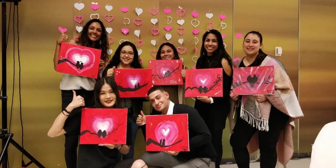 Group of guests holding finished heart-themed canvas paintings at an indoor guided painting workshop