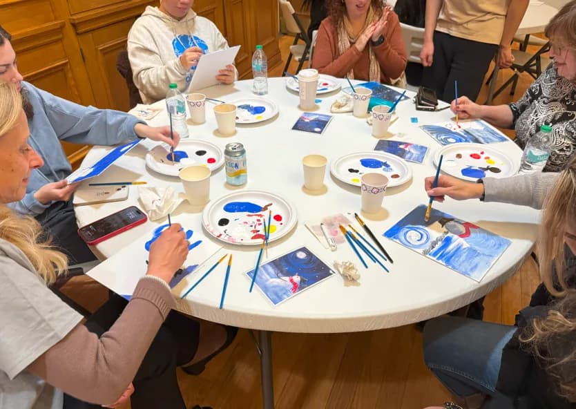 Overhead view of guests painting blue and white canvases together at a round table during a guided painting workshop