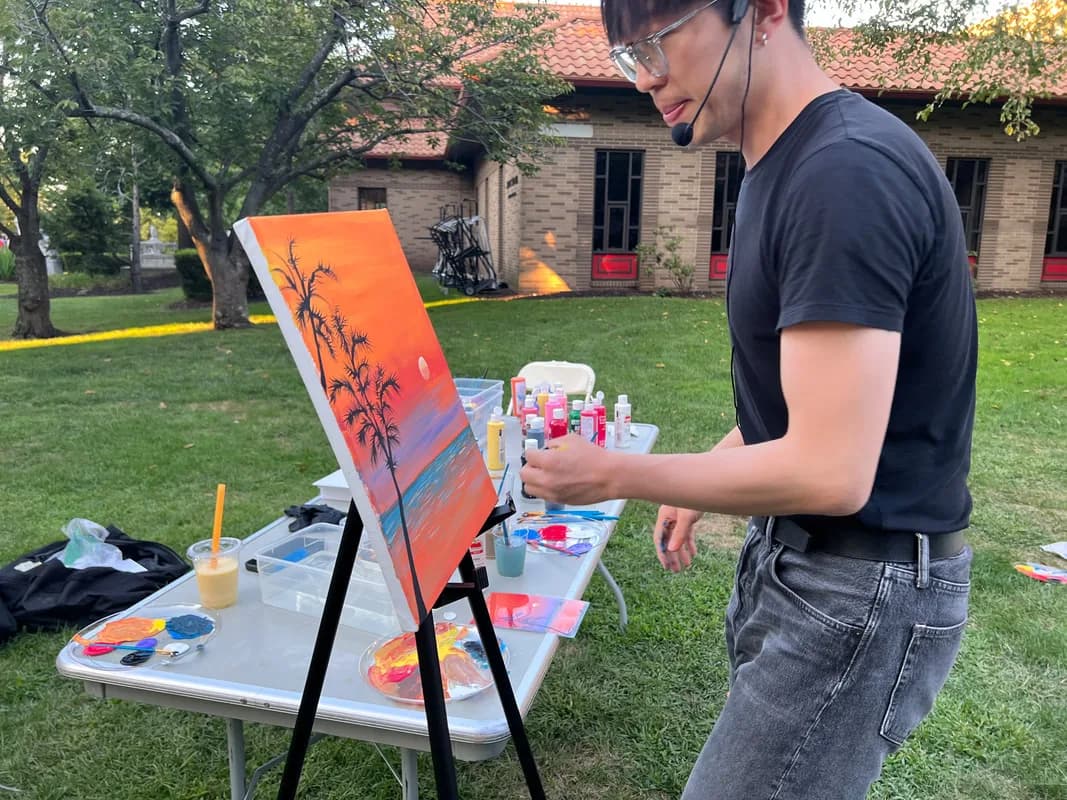 Instructor painting a sunset palm tree canvas outdoors at a guided painting workshop