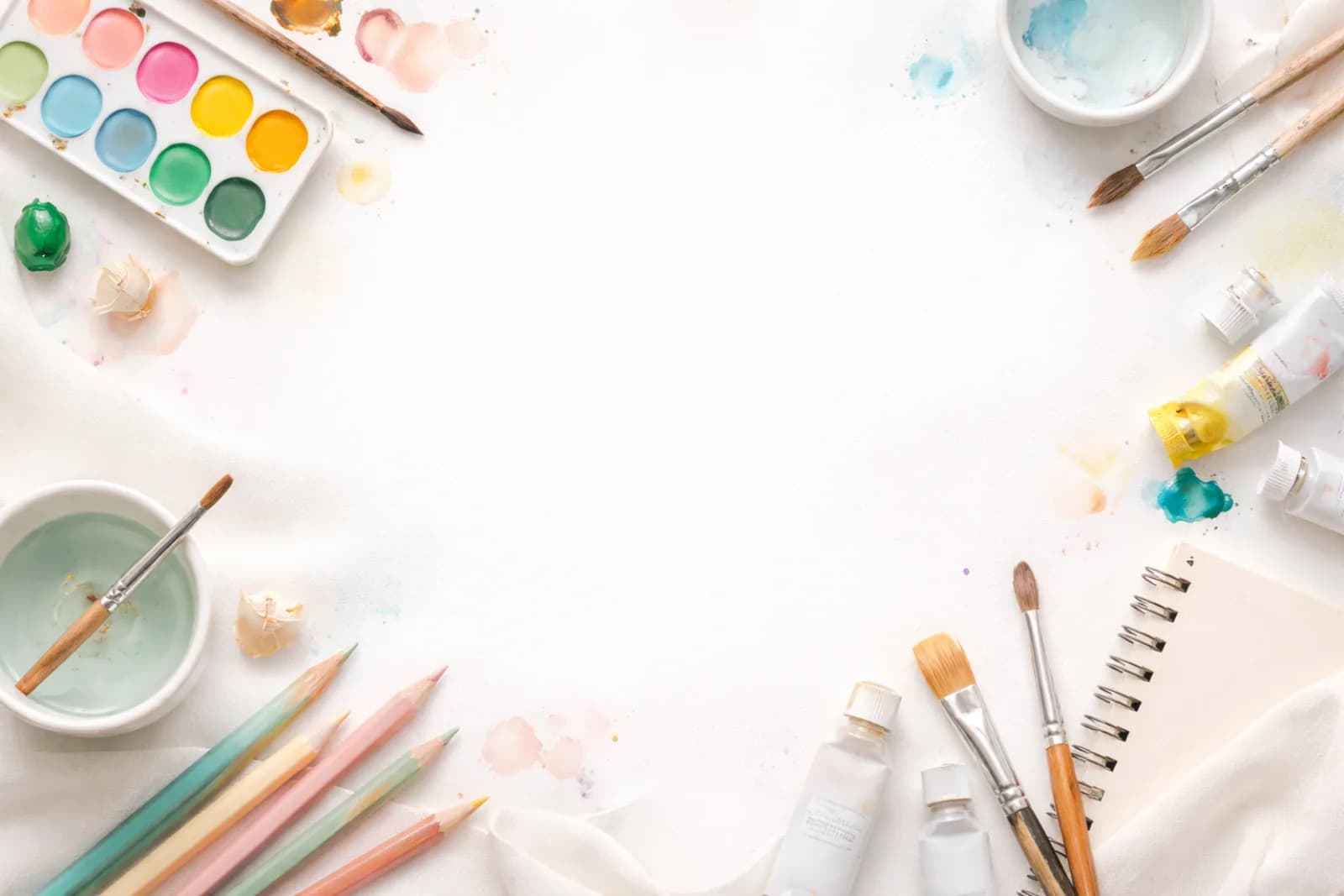 Paintbrushes, watercolors, and colored pencils arranged around a blank canvas at the painting workshop