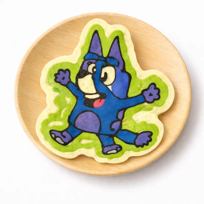 Pancake art shaped into a blue cartoon dog character with arms raised at a kids event pancake station