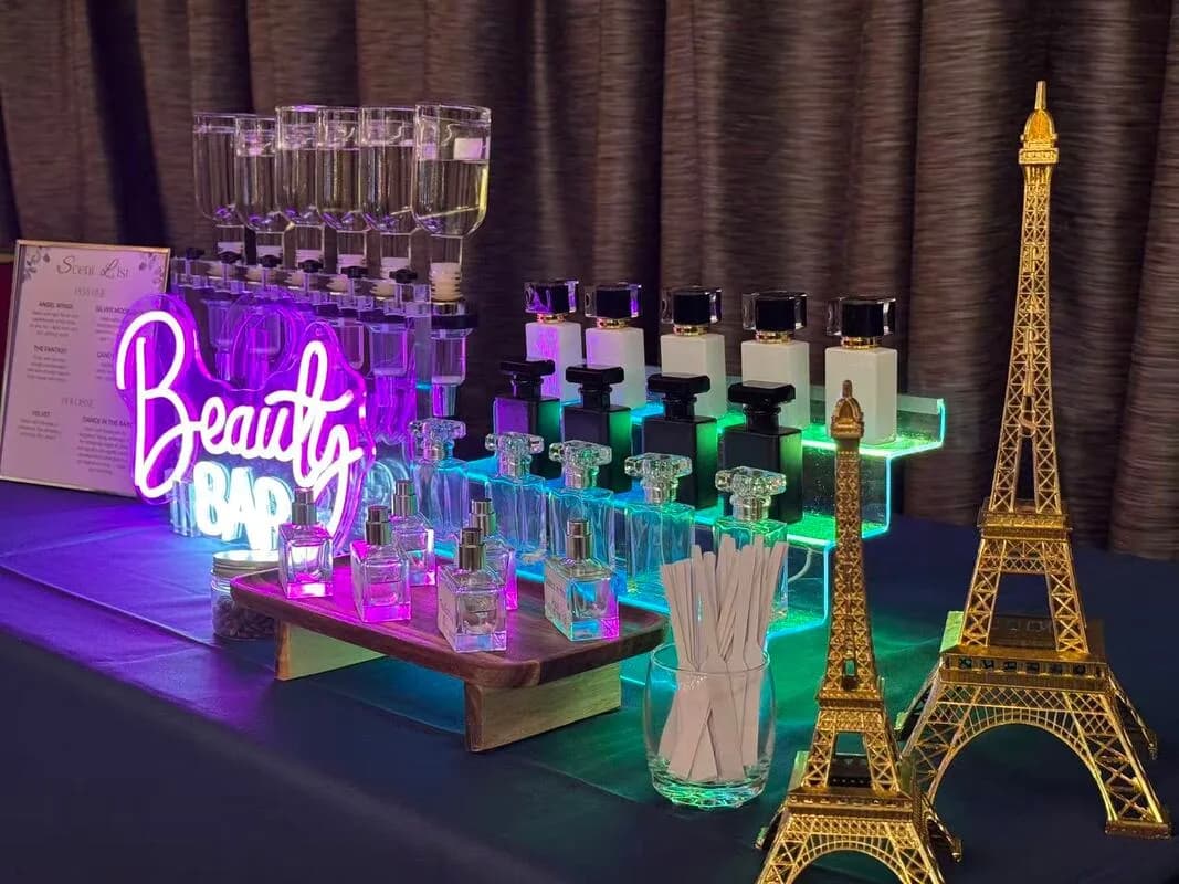 Elegant perfume bar setup with a lit Beauty Bar sign, bottle dispensers, and gold Eiffel Tower decor at an event