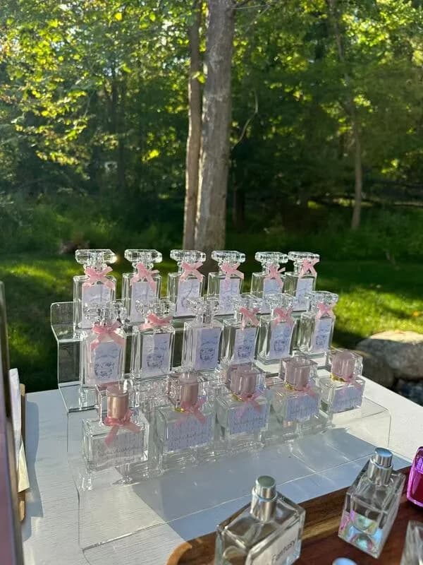 Rows of bottled perfume with pink ribbon accents displayed outdoors at a daytime perfume bar station