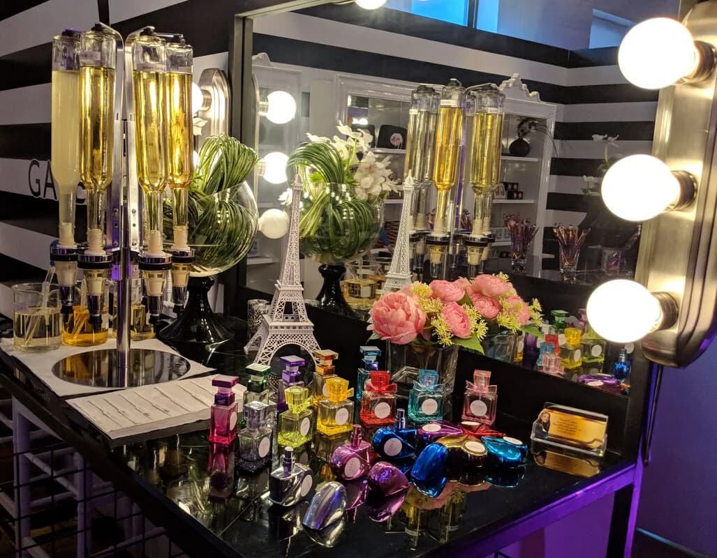 Colorful bottled fragrances and dispensers arranged at a mirrored vanity with a gold Eiffel Tower accent