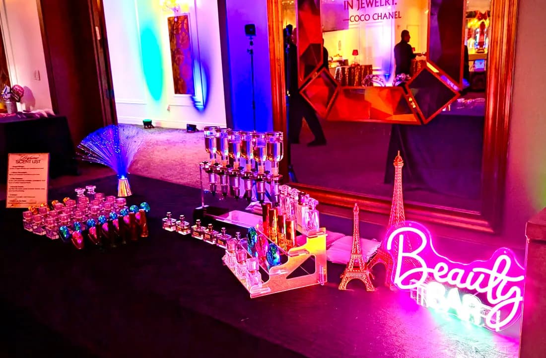 Glowing pink Beauty Bar neon sign beside a fragrance scent list and gold Eiffel Tower decor at an evening event