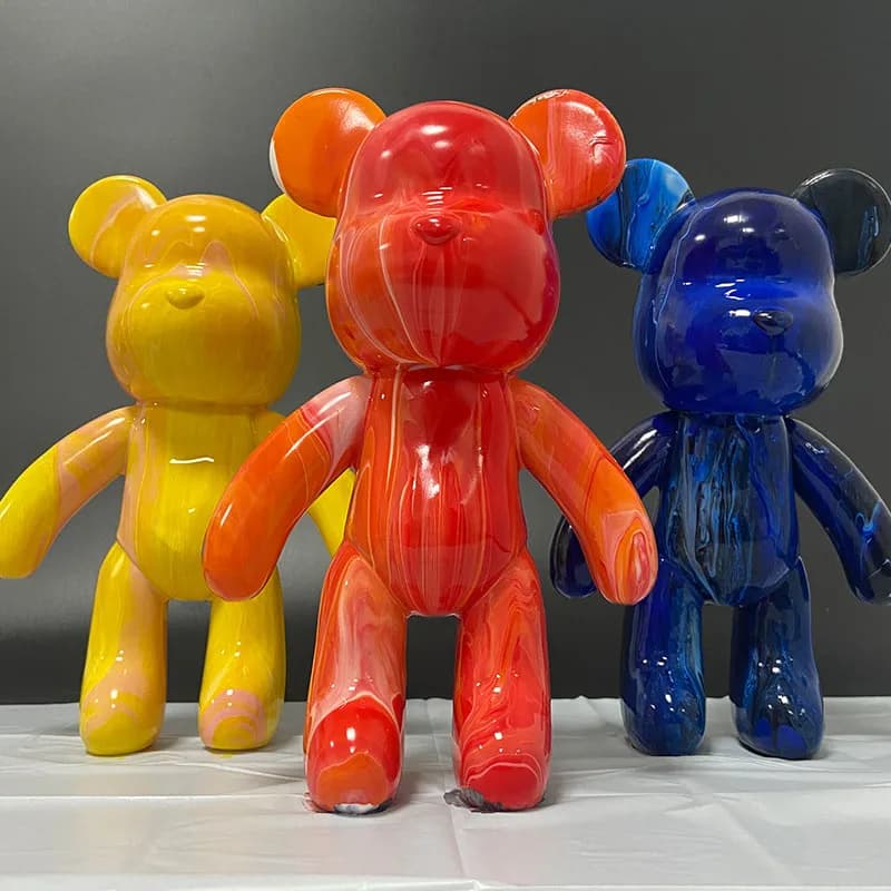 Three finished pour-paint bear figures in yellow, red, and blue displayed together from the rainbow bears station