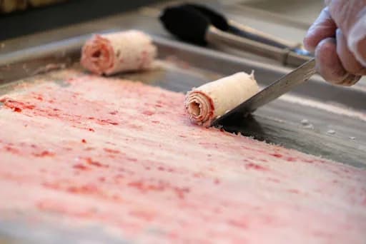 Ice cream base being scraped into tight rolls on a frozen slab at an event rolled ice cream station