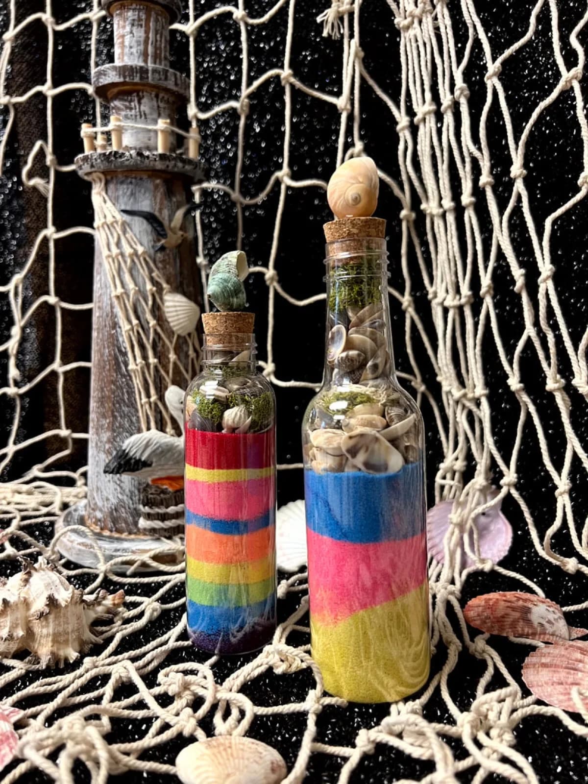 Two glass bottles with layered colored sand and small shells sealed inside with cork stoppers at a sand art station