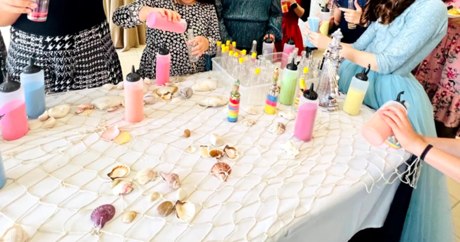 Guests filling glass bottles with colored sand at a styled sand art station table decorated with seashells