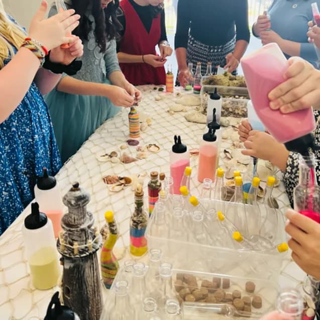 Overhead view of guests layering colored sand into bottles at a styled sand art station table decorated with seashells