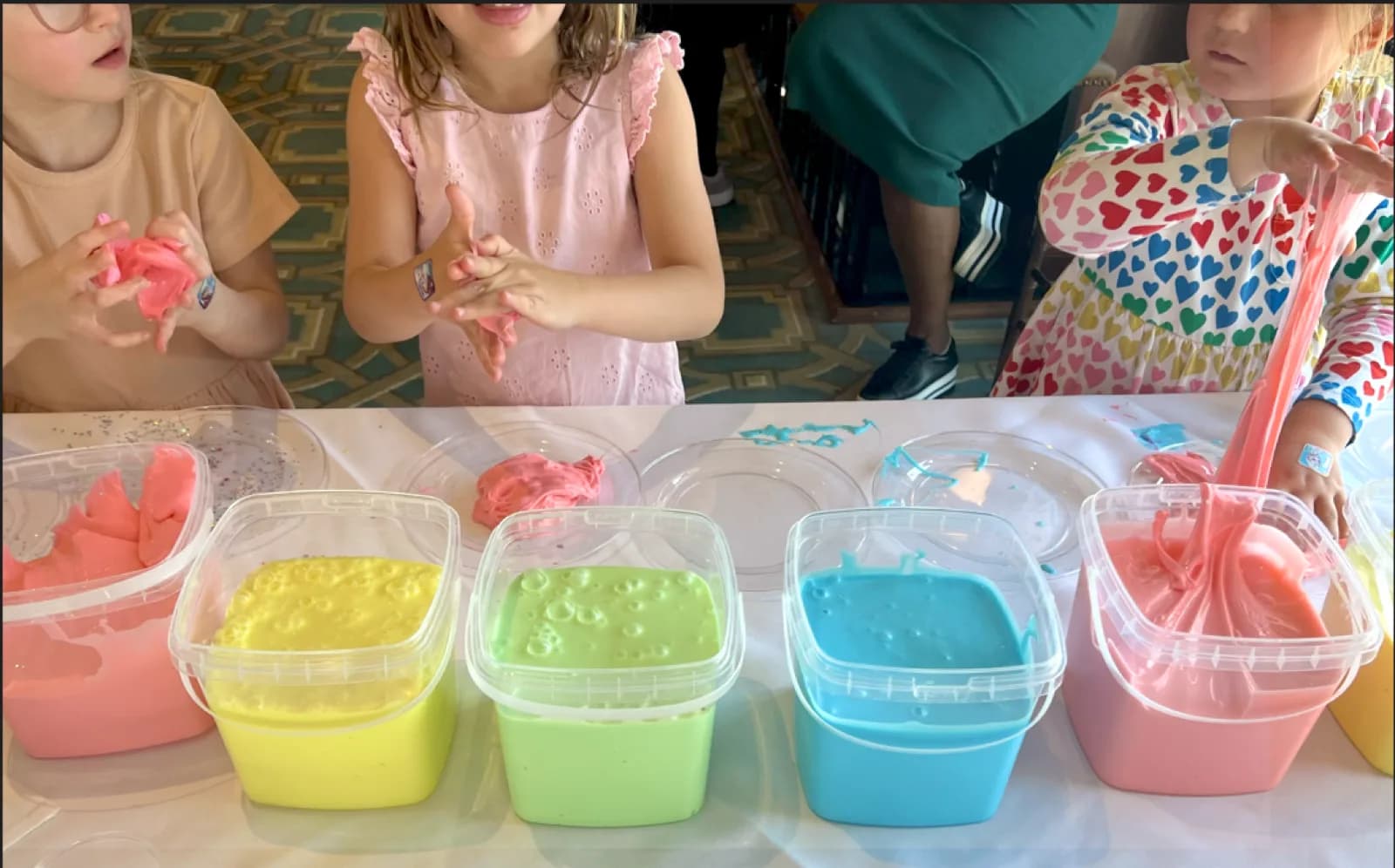 Kids mixing and stretching colorful slime together at a hands-on slime bar station