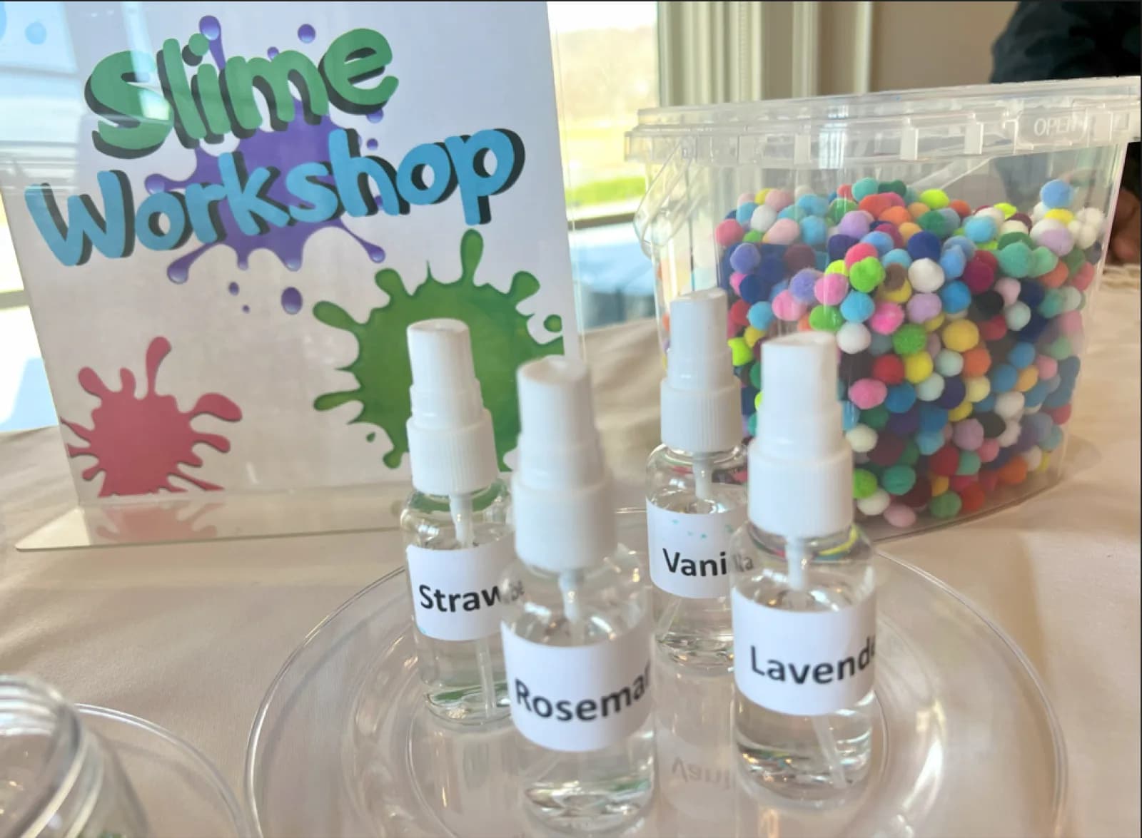 Slime bar station scent display with labeled fragrance sprays and a bin of mini pom-poms for mix-ins